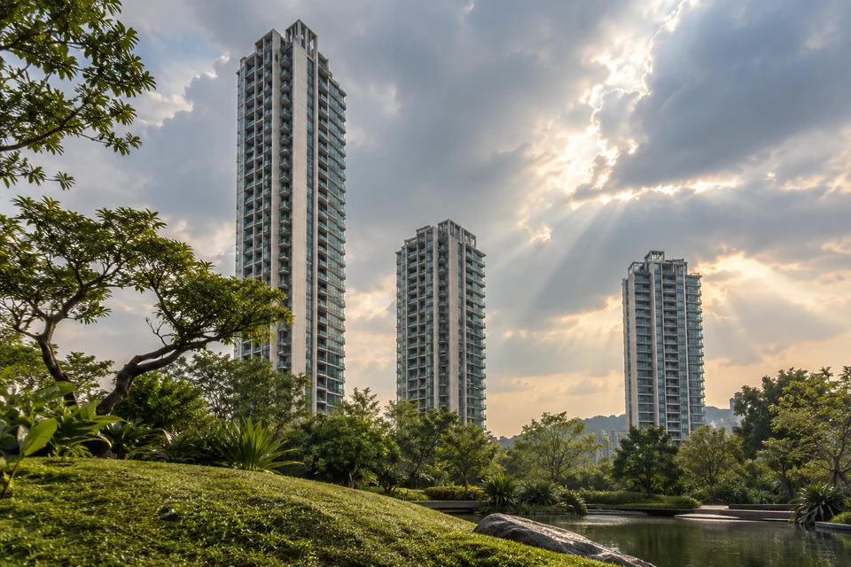 灵感图景：低机位越过湿润草坡，看到三座高低不同的住宅塔楼，云缝日光勾勒银色边线。